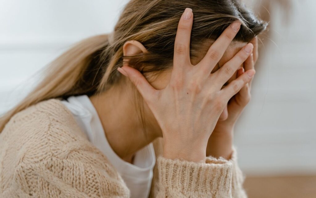 Frau mit Kopf in den Händen – Symbol für Stress, Überforderung und Trauma, die das Nervensystem aus dem Gleichgewicht bringen.